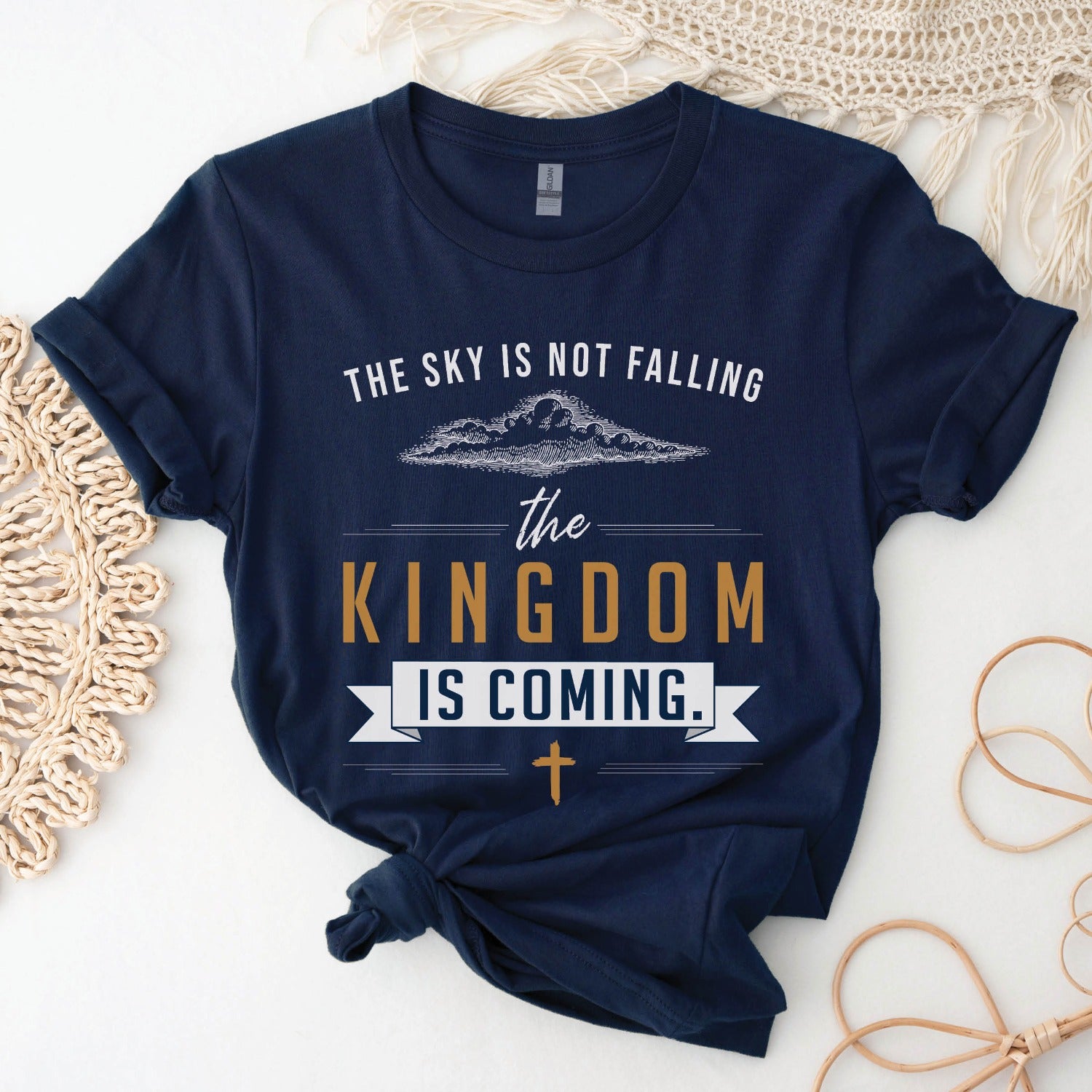 Navy blue unisex t-shirt with a Christian Kingdom of God through Jesus faith-based message that says, "The Sky Is Not Falling, The Kingdom is Coming" with bold font, vintage clouds, banner, and cross design in white and gold, created for bible study Men and Women believers, 2024 eclipse