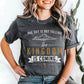 Trendy young woman wearing a heather dark gray unisex t-shirt with a Christian Kingdom of God through Jesus faith-based message that says, "The Sky Is Not Falling, The Kingdom is Coming" with bold font, vintage clouds, banner, and cross design in white and gold, created for bible study Men and Women believers, 2024 eclipse