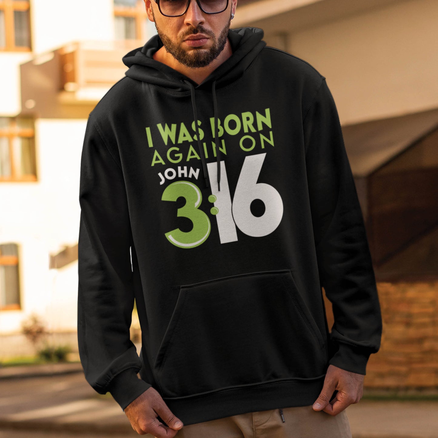 Trendy man wearing a Black Unisex Cozy Hoodie with Christian aesthetic bible verse message that says, "I Was Born Again On John 3:16" bible verse quote in lime green and white for men and women