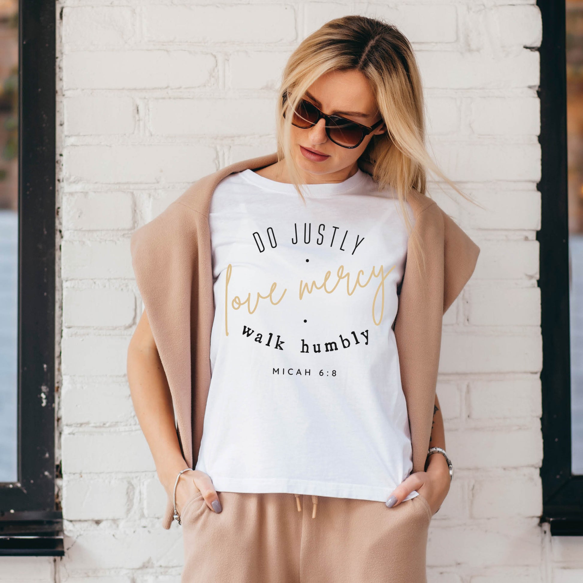 Woman wearing a white Christian aesthetic faith-based unisex t-shirt for women with Micah 6:8 bible verse scripture printed that says, Do Justly Love Mercy walk humbly, in gold and black, unique gift for her