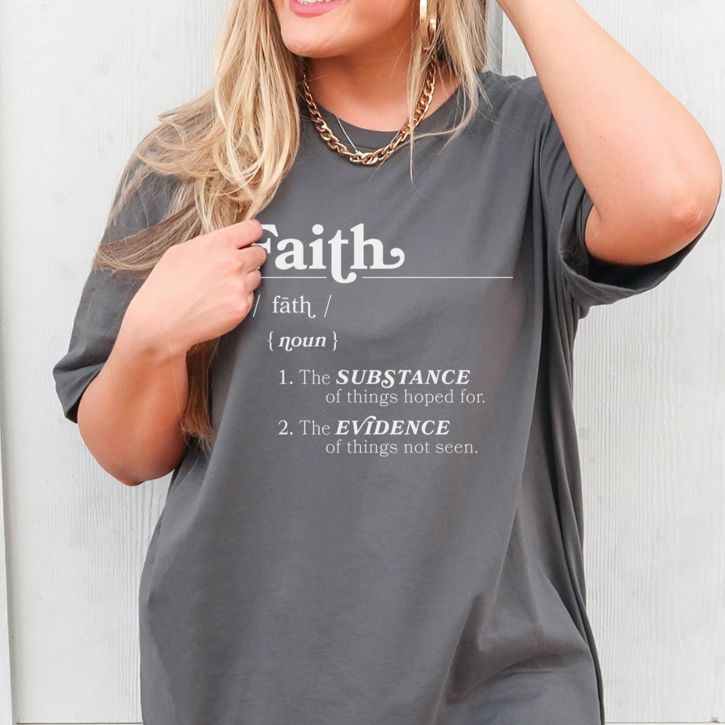 Young woman wearing a Faith Definition Hebrews 11:1 Christian aesthetic design printed in white on soft oversized asphalt gray unisex t-shirt for women and men