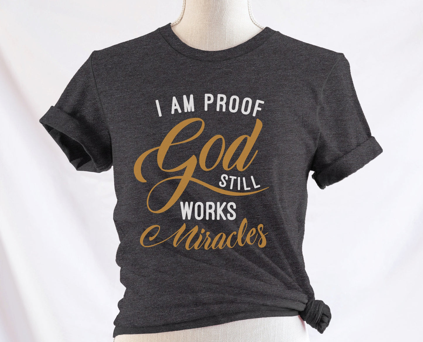 I am proof God still works miracles Christian aesthetic testimony design printed in white and gold on soft heather dark gray unisex t-shirt for women