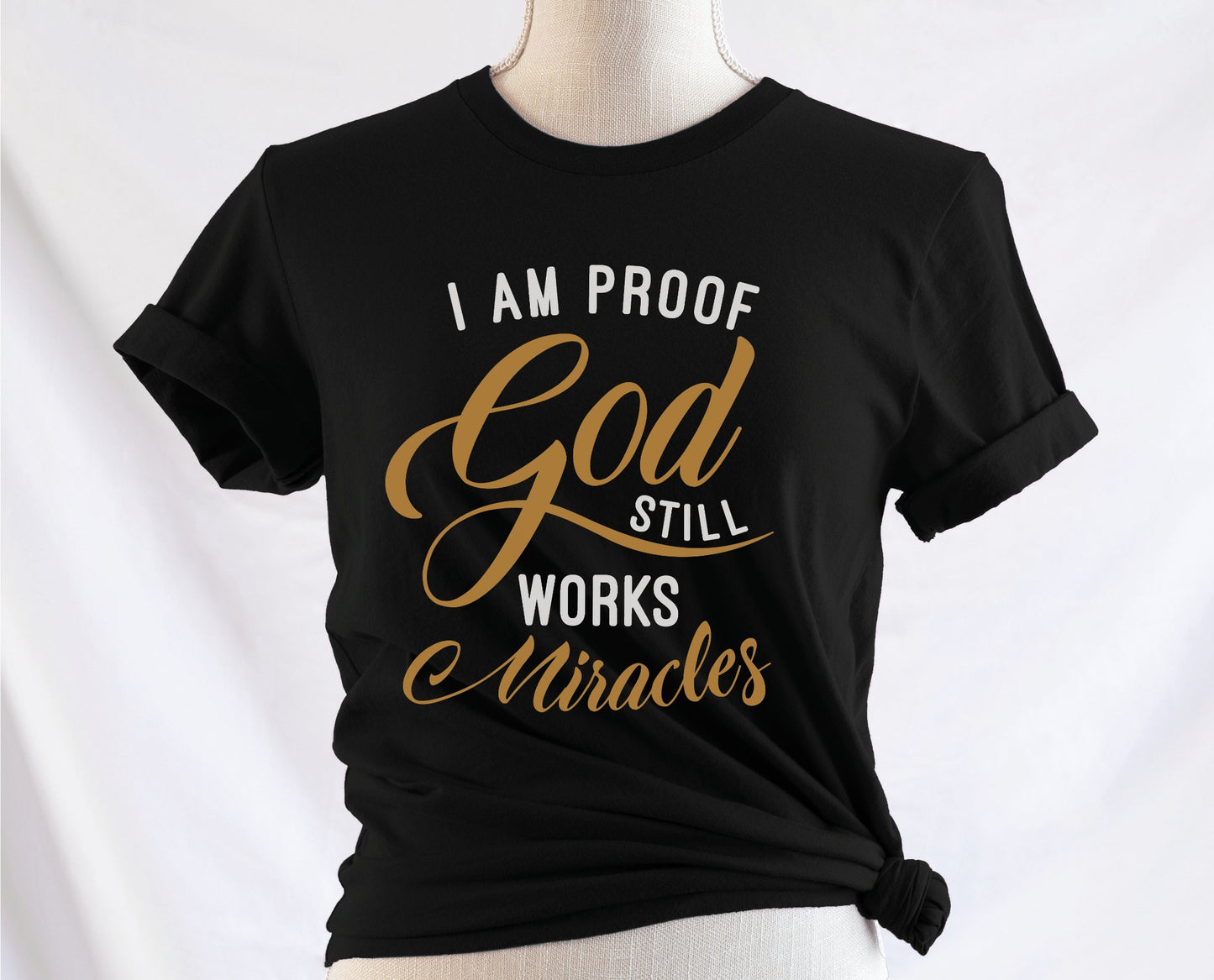 I am proof God still works miracles Christian aesthetic testimony design printed in white and gold on soft black unisex t-shirt for women