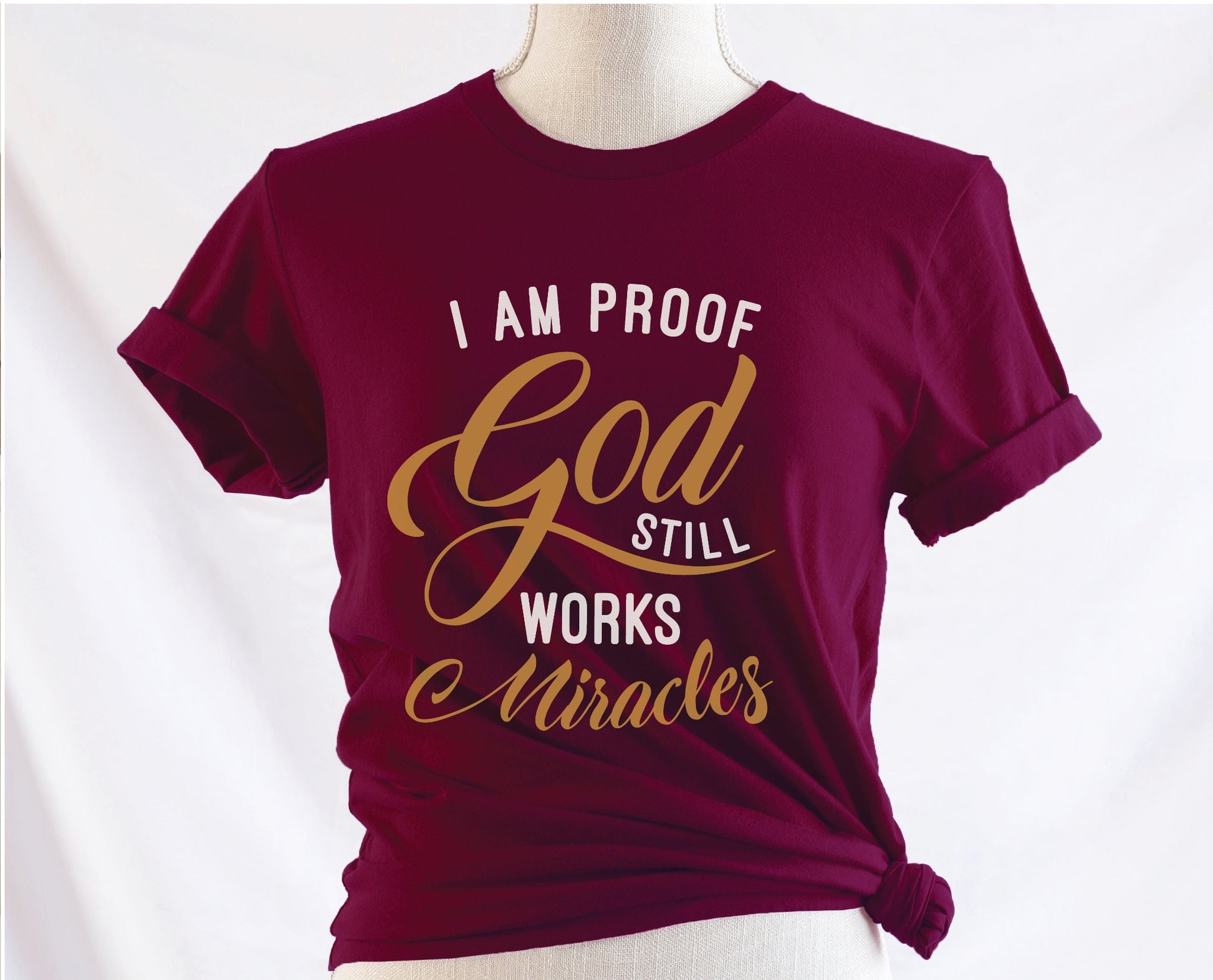 I am proof God still works miracles Christian aesthetic testimony design printed in white and gold on soft maroon unisex t-shirt for women
