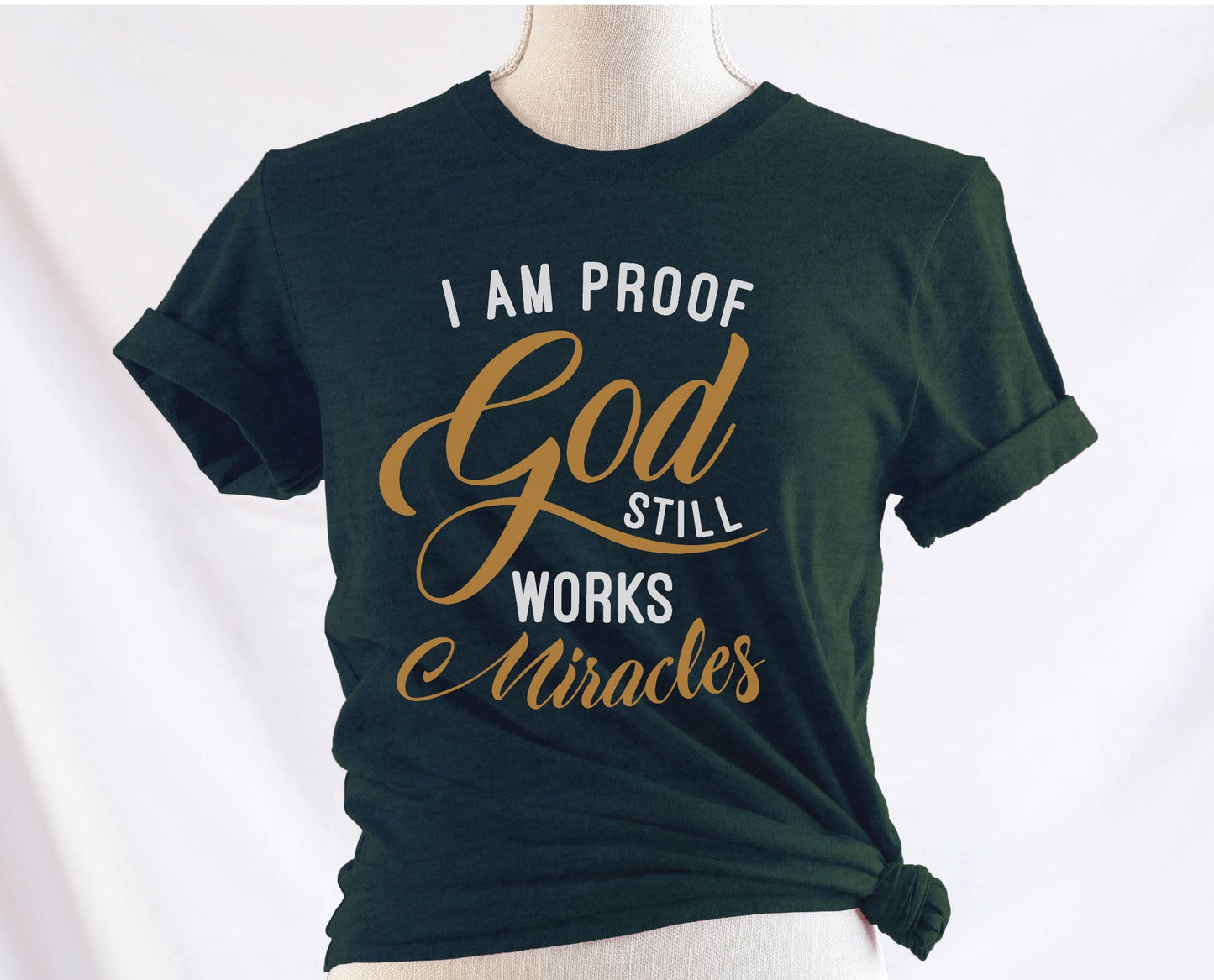 I am proof God still works miracles Christian aesthetic testimony design printed in white and gold on soft heather forest green unisex t-shirt for women