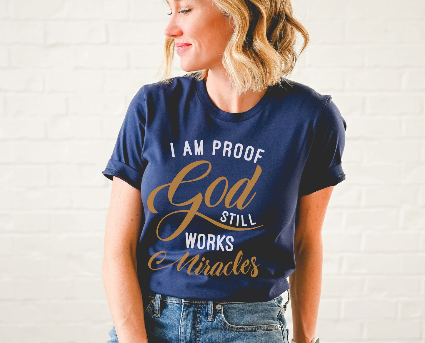 I am proof God still works miracles Christian aesthetic testimony design printed in white and gold on soft navy blue unisex t-shirt for women