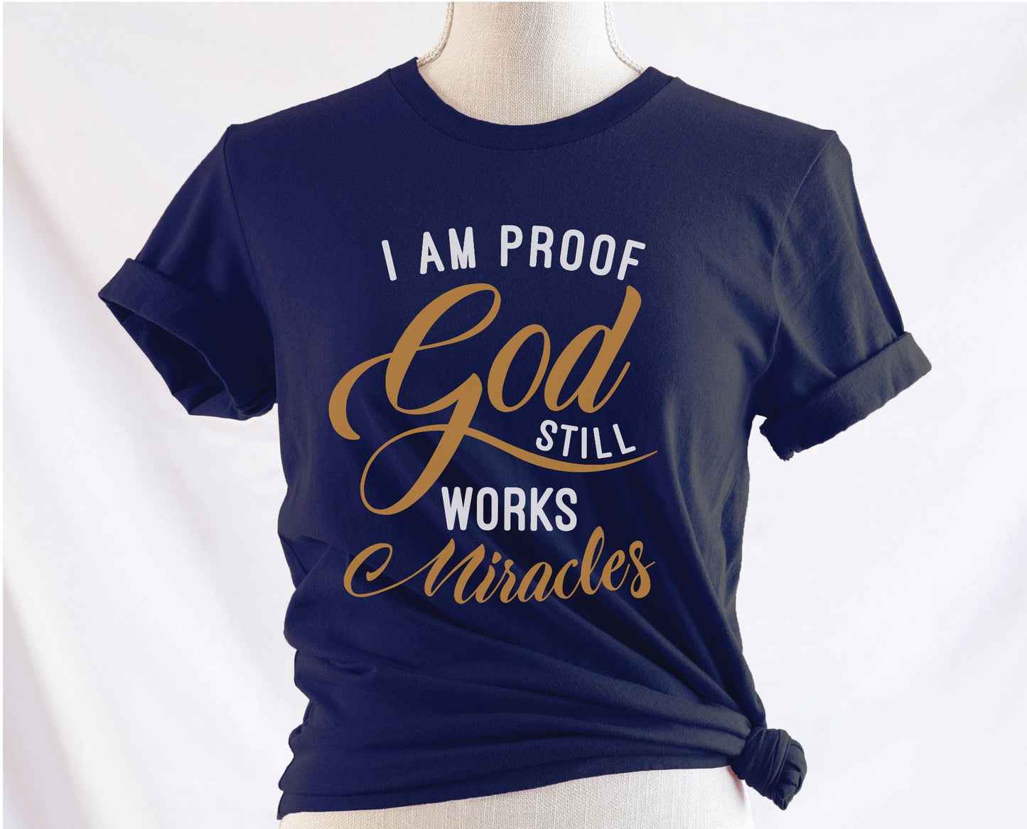 I am proof God still works miracles Christian aesthetic testimony design printed in white and gold on soft navy blue unisex t-shirt for women
