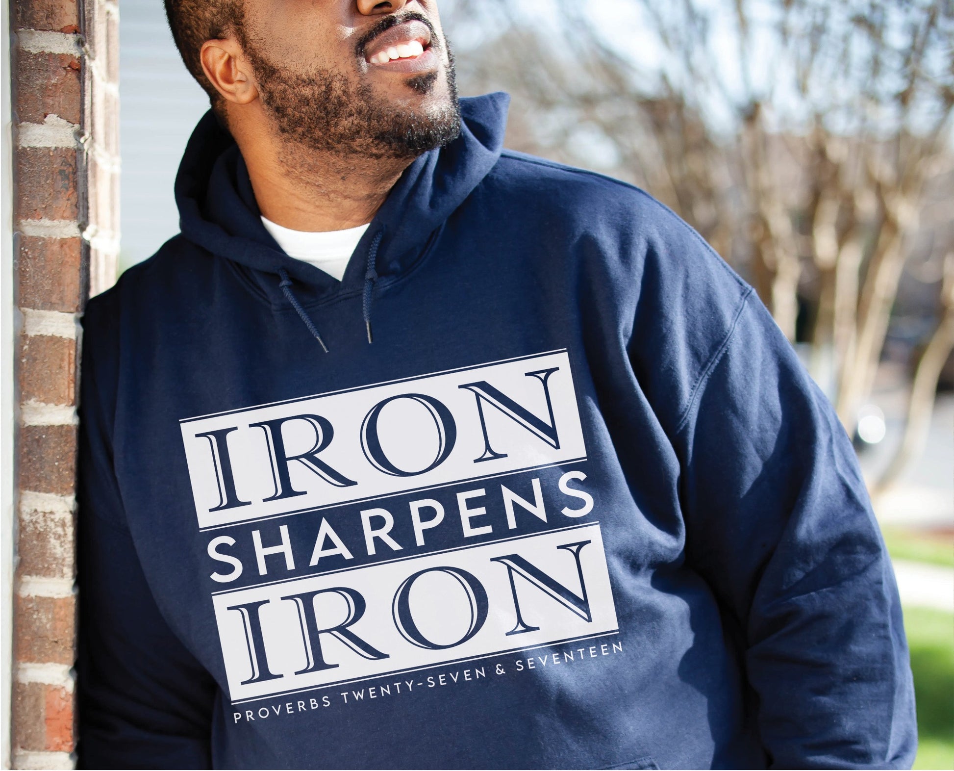 Young black man wearing an Iron Sharpens Iron Proverbs 27:17 Bible Verse Christian aesthetic faith-based hoodie with bold white design printed on cozy navy blue unisex hoodie sweatshirt for men and women