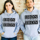 Young man and woman couple wearing Iron Sharpens Iron Proverbs 27:17 Bible Verse Christian aesthetic faith-based hoodie with bold black design printed on cozy heather sport gray unisex hoodie sweatshirt for men and women