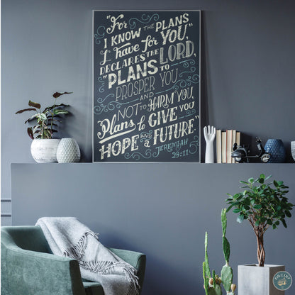 A 16x20" canvas wall art print featuring the text of Jeremiah 29:11 Bible verse in  cream and teal color typography and hand drawn swirl design elements with a moody navy blue background for home, church, or office decor, presented propped upon a shelf in a modern living room against a beautiful smoky blue wall