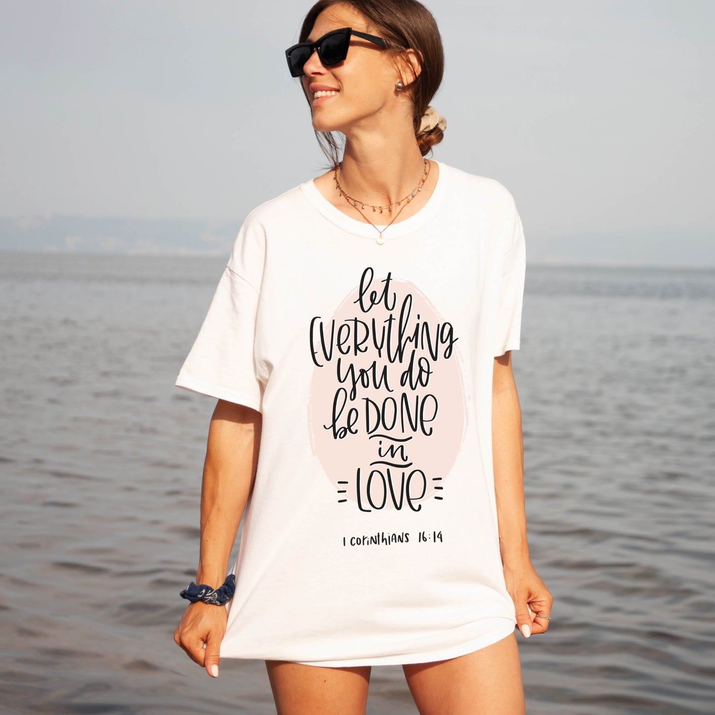 Young woman walking in lake with soft quality white t-shirt swimsuit cover up with 1 Corinthians 16:14 Let Everything You Do Be Done In Love bible verse printed in blush pink and black - Christian aesthetic unisex tee shirt design for women