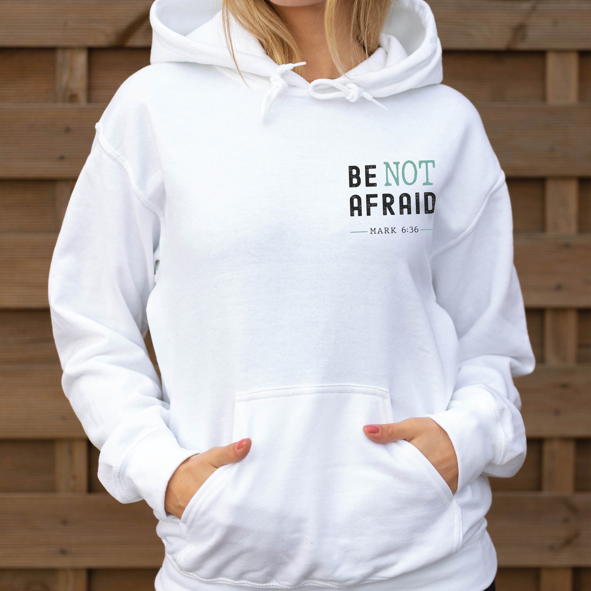 Young woman wearing a Do Not Be Afraid Only Believe Jesus Quote Mark 5:36 healing miracle bible verse Christian aesthetic textured black and teal printed on front and back of cozy white unisex hoodie sweatshirt for men and women
