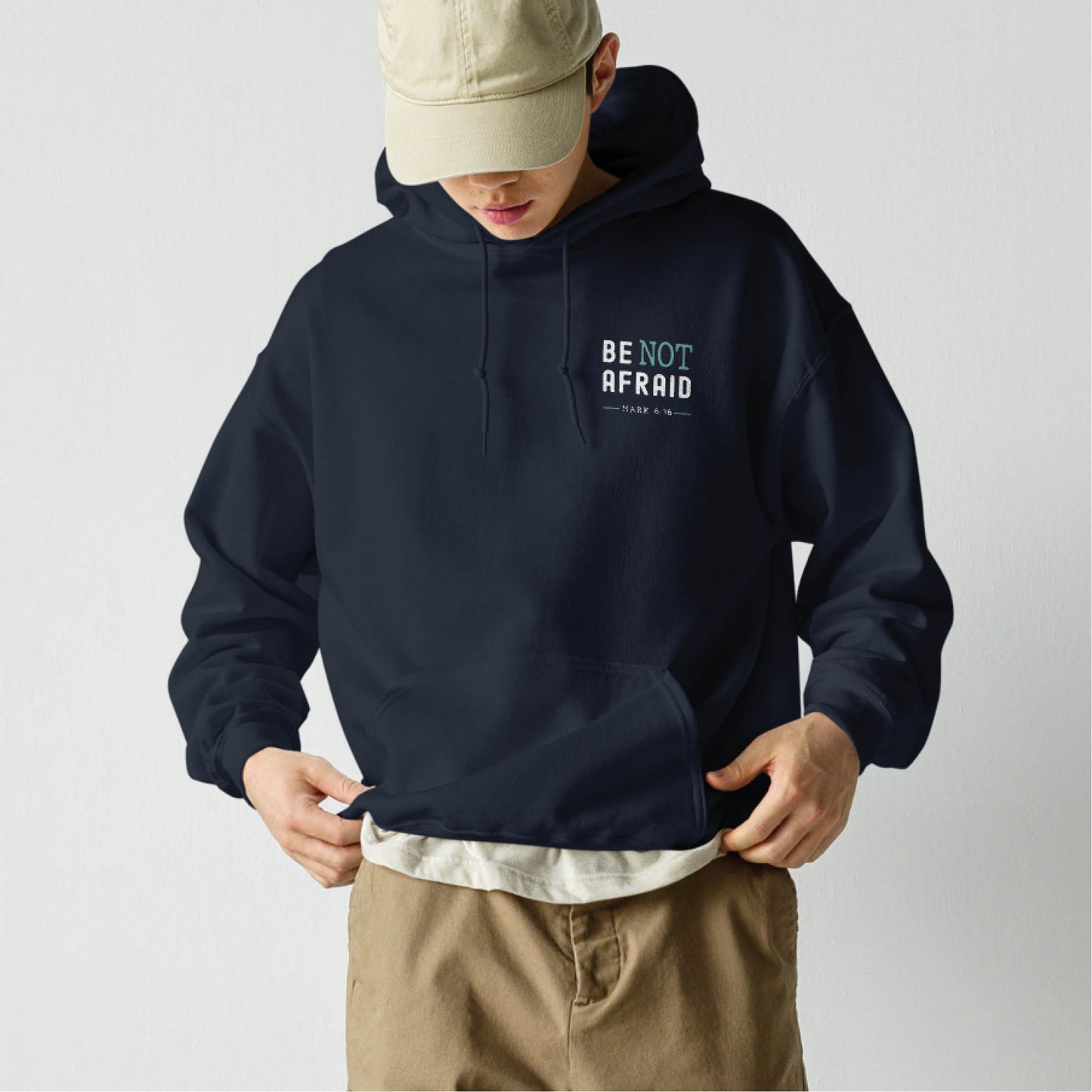 Young man wearing a Do Not Be Afraid Only Believe Jesus Quote Mark 5:36 healing miracle bible verse Christian aesthetic textured black and teal printed on front and back of cozy navy blue unisex hoodie sweatshirt for men and women