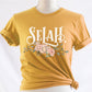 Selah Psalm bible verse watercolor floral Christian aesthetic design printed in white peach blush pink on soft mustard yellow t-shirt for women